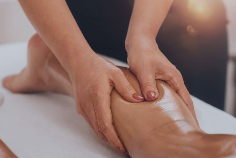 Primer plano de manos realizando un masaje con aceites sobre la pierna de una persona, enfocado en la relajación muscular y el bienestar físico; imagen representativa de los servicios corporales en Caminar Creciendo, Sevilla.